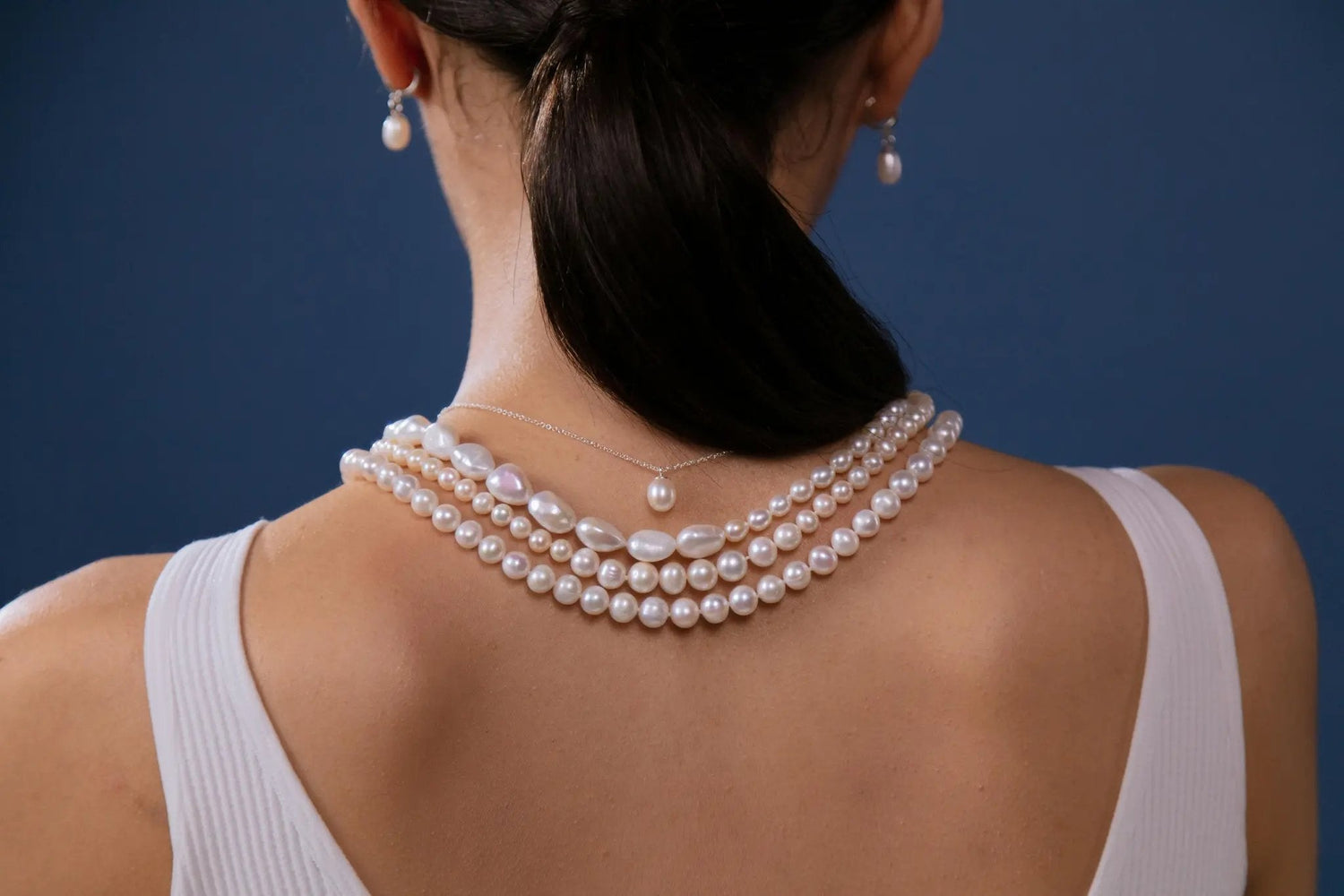 Woman's back displaying multiple white pearl necklaces and pearl pendant.